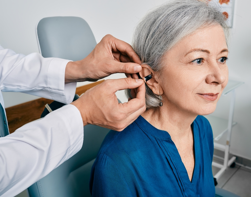woman during installation hearing aid into her ear by her audiologist
