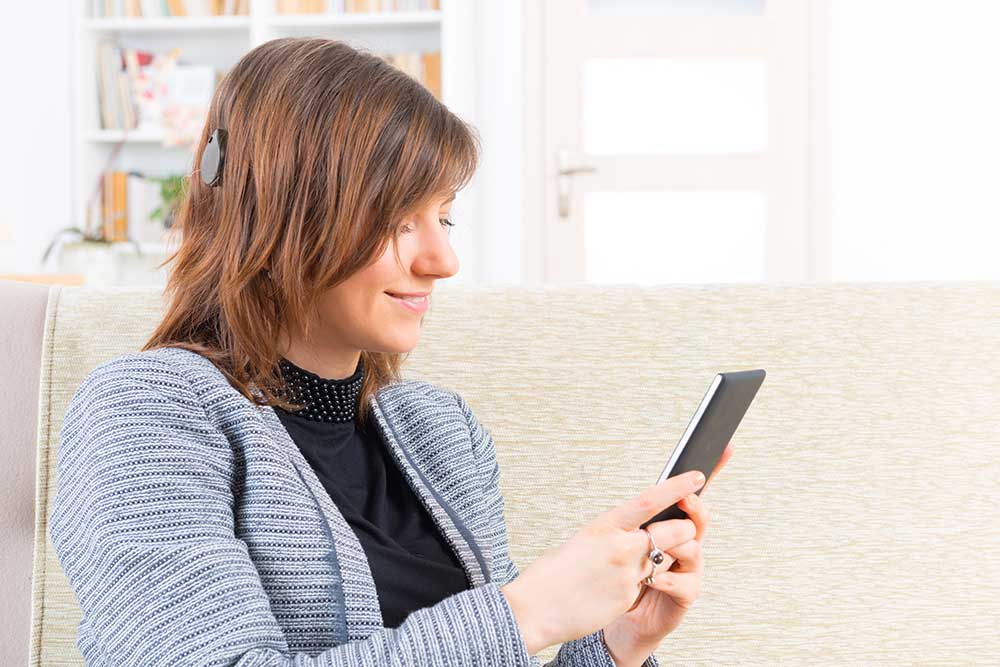 Woman with cochlear implants sitting on the couch smiling at something on her phone